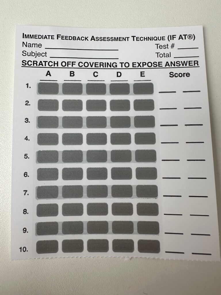 A photo of a blank Immediate Feedback Assessment Technique sheet, consisting of 10 questions each with 5 boxes to scratch, labelled A to E. There is a space after each question for a score. At the top of the page is a space for student name, subject, test number and total score.