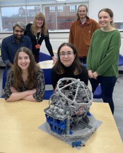 A photo of Vicky Fawcett and five of her colleagues standing or sitting behind a table on which sits a Lego model of the Extremely Large Telescope