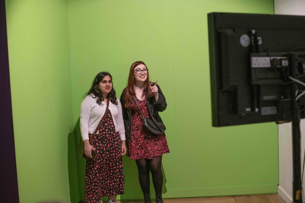 Two visitors standing in front of a green screen.