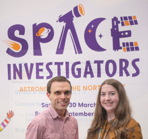 A photograph of Vicky Fawcett and a colleague, standing in front of a Space Investigators Poster