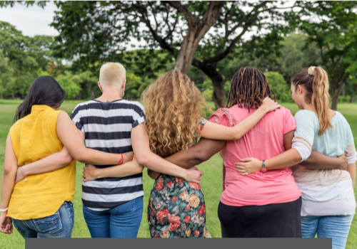 Five women walking in grass with their arms around each other